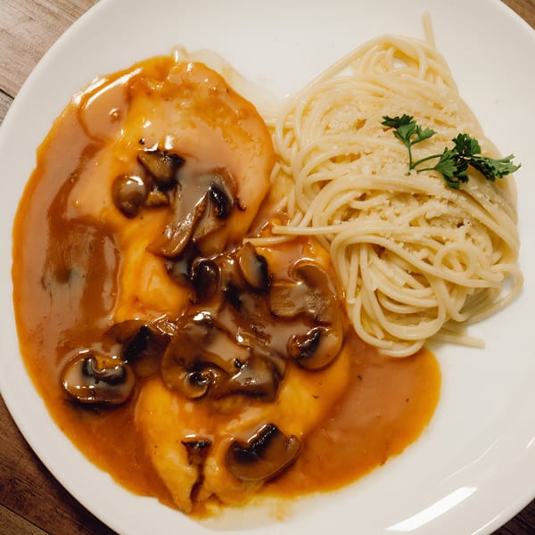Chicken Marsala with mushrooms and gravy, served with a side of spaghetti and parsley.