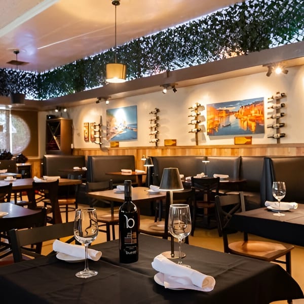 Volare Restaurant's dining room with set tables, booths, and wine bottle displays on the walls.