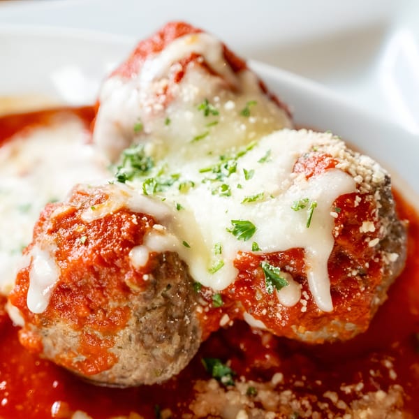 Three meatballs covered in marinara sauce, melted mozzarella, parmesan, and fresh parsley.