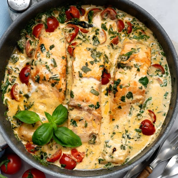 Creamy Tuscan salmon with spinach, cherry tomatoes, and basil in a pan.