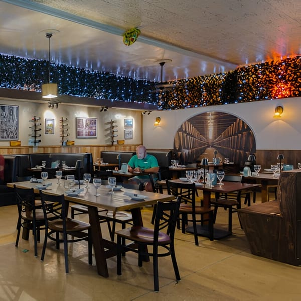 Volare Restaurant dining room with tables set, a man seated, and decorative lighting on the walls.