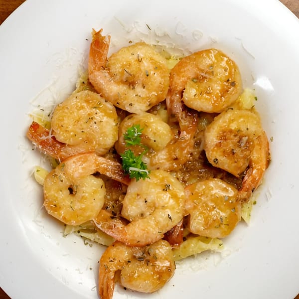 Close-up of golden-brown shrimp scampi with herbs and grated cheese on a white plate.