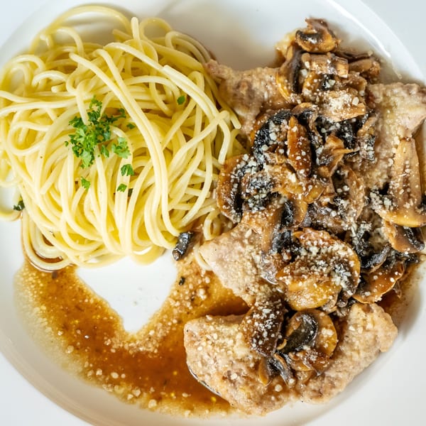 Veal scallopini with mushroom sauce and spaghetti, garnished with parsley, on a white plate.
