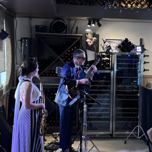 A man playing guitar and a woman holding a saxophone perform on a stage at Volare Restaurant.