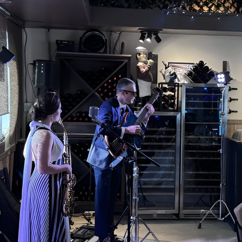 A man playing guitar and a woman holding a saxophone perform on a stage at Volare Restaurant.